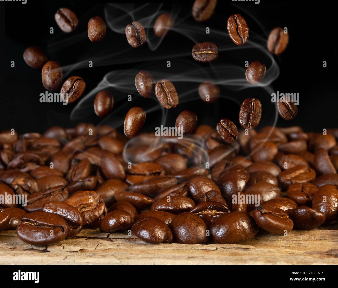 chicchi di caffè torrefatti caldi con vapore su sfondo nero e legno Foto Stock