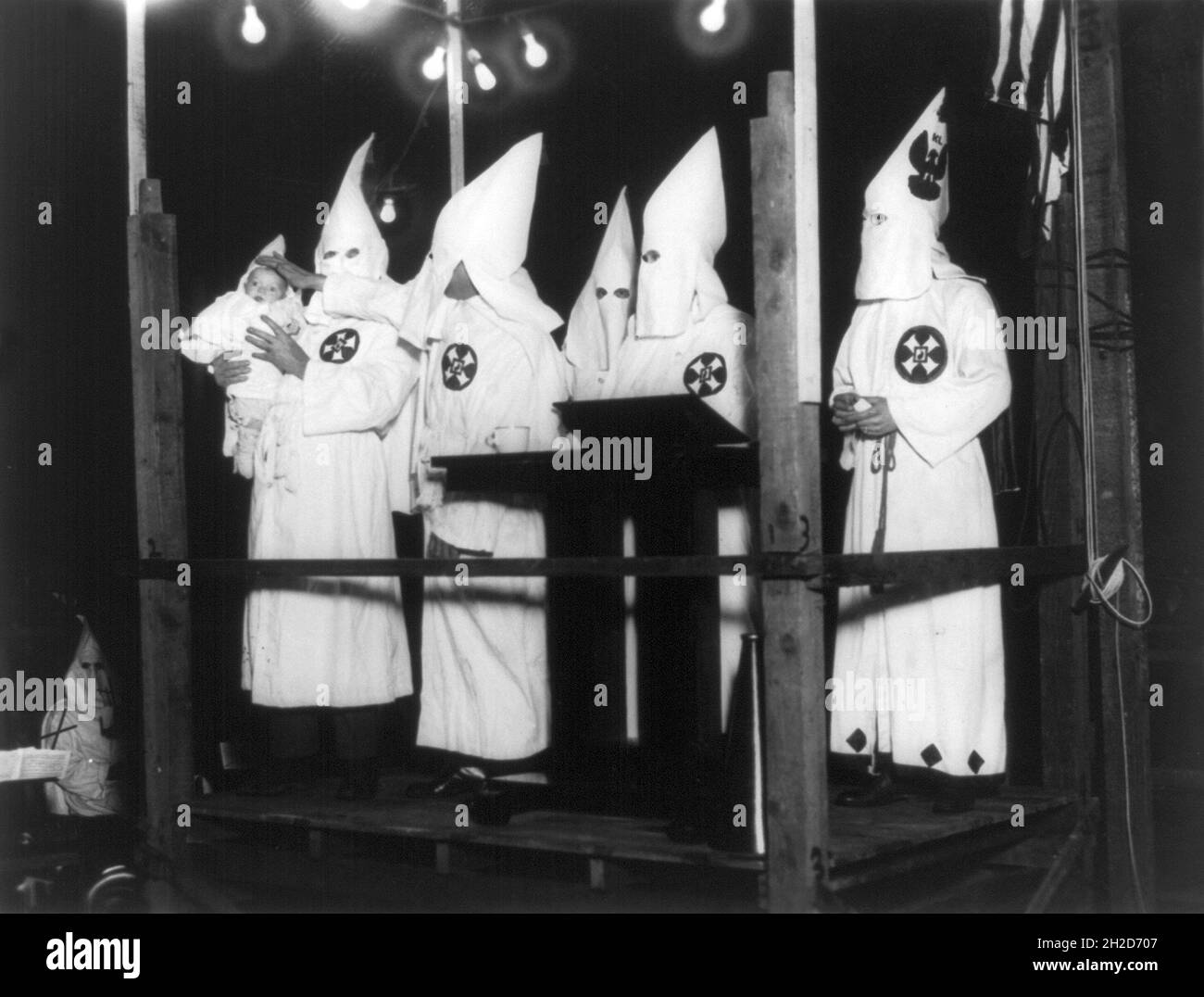 Foto d'epoca circa 1924 che mostra i membri del Ku Klux Klan che batte un bambino di 8 settimane vestito anche in Ku Klux Klan accappatoi di fronte ad un altare Foto Stock Foto d'epoca circa 1924 che mostra i membri del Ku Klux Klan che batte un bambino di 8 settimane vestito anche in Ku Klux Klan accappatoi di fronte ad un altare Foto Stock