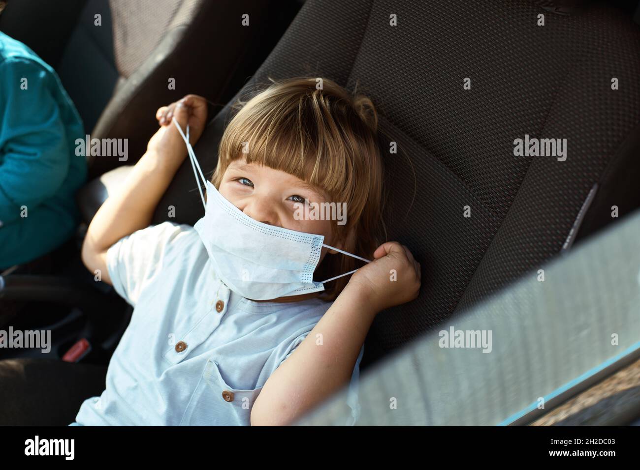 Il bambino si siede sul sedile in auto, ride e mette su una maschera Foto Stock