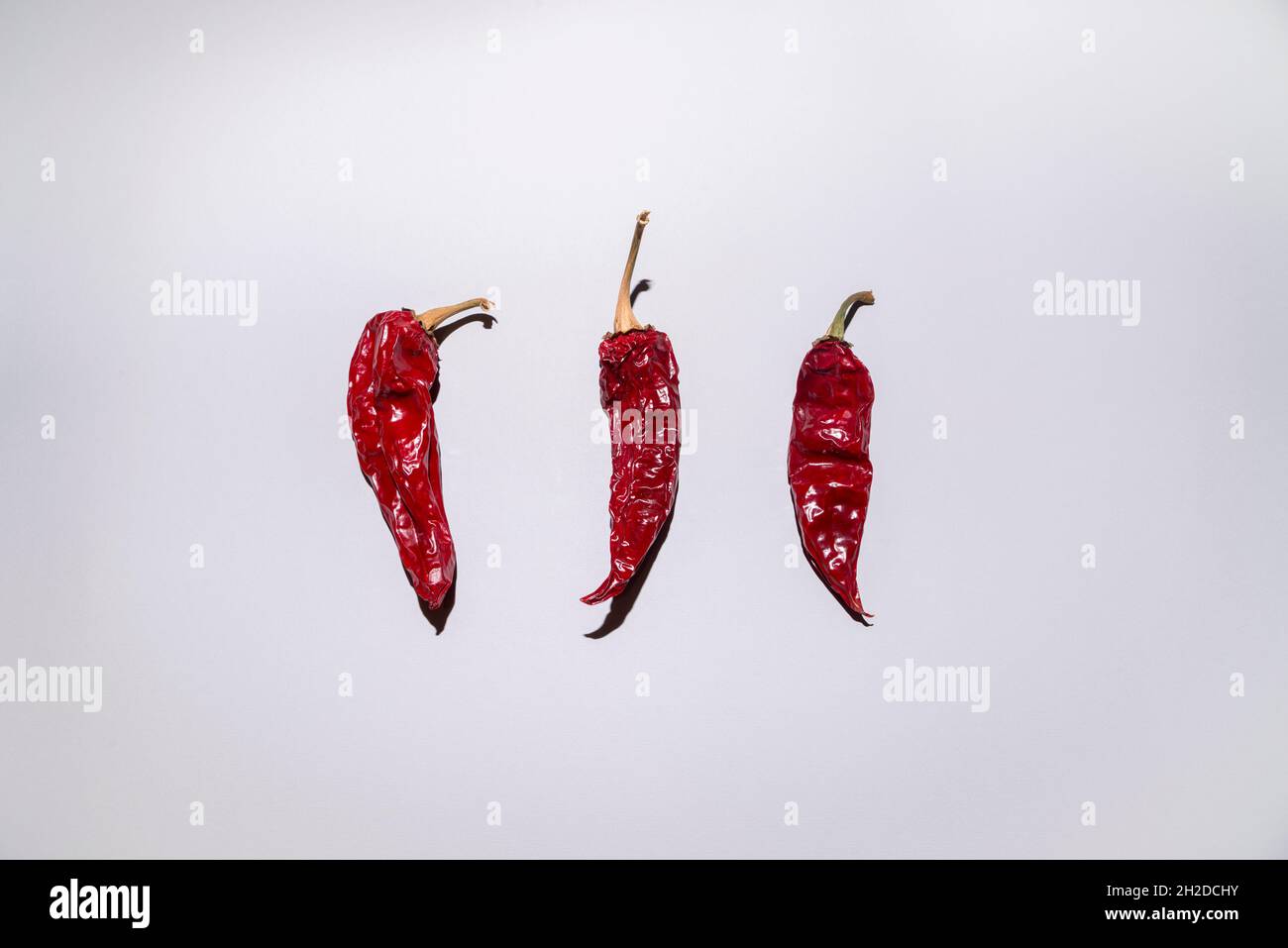 Layout creativo composto da tre peperoni rossi su sfondo grigio. Vista dall'alto, piatto. Cibo minimo e concetto specifico di stagione. Foto Stock