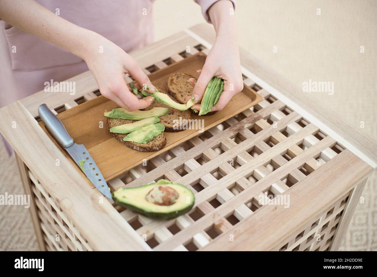 Il grandangolo della giovane donna mette la fetta di avocado sul pane Foto Stock