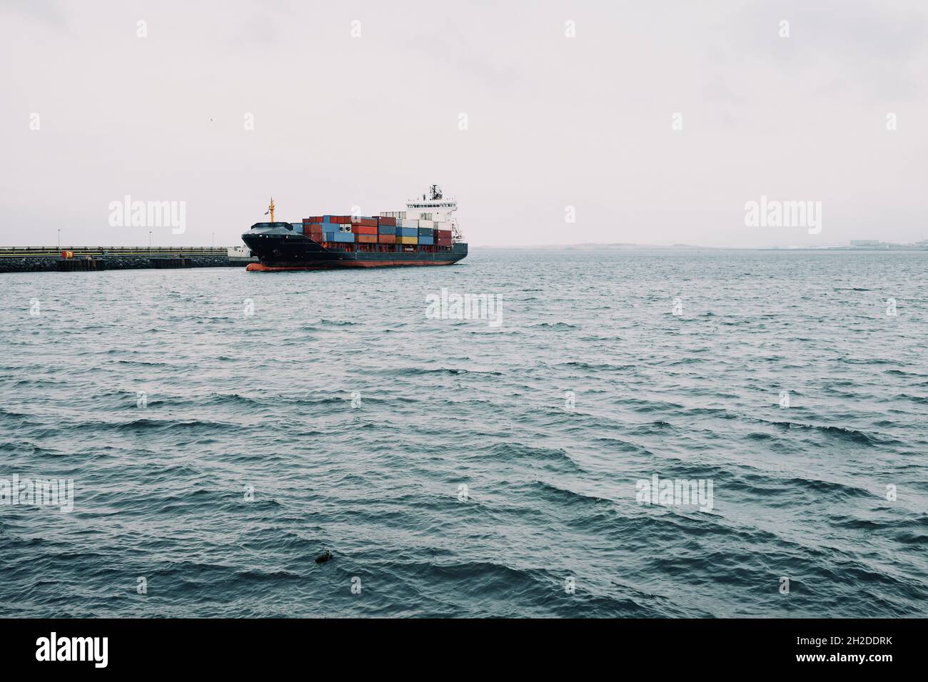 Nave industriale con cumuli di container su mare ondulato con molo sotto cielo nuvoloso nel porto d'Islanda Foto Stock