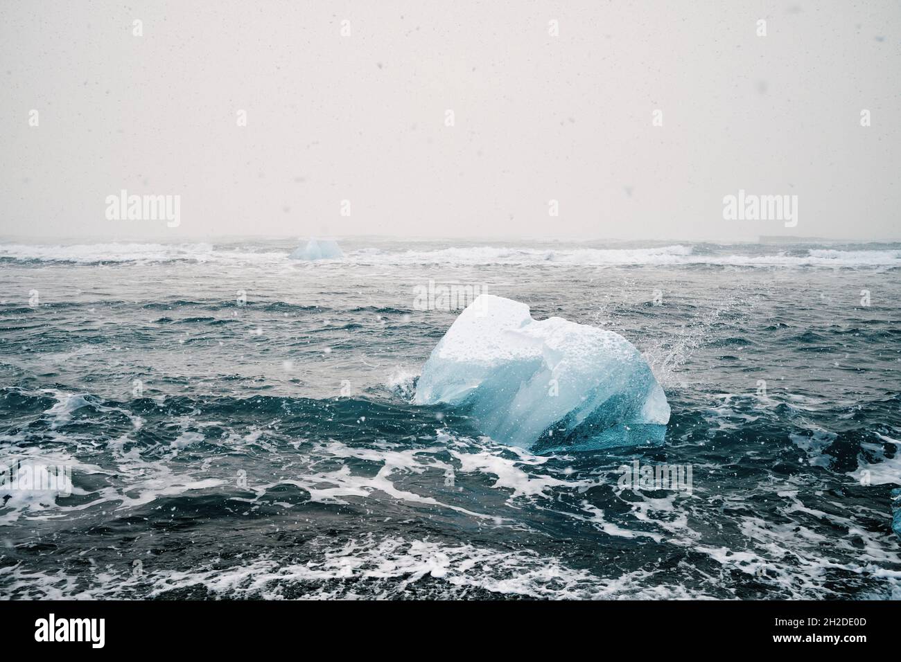 Vista pittoresca del pezzo di ghiaccio nell'oceano ondulato con fluidi d'acqua schiumosi sotto il cielo chiaro in Islanda Foto Stock
