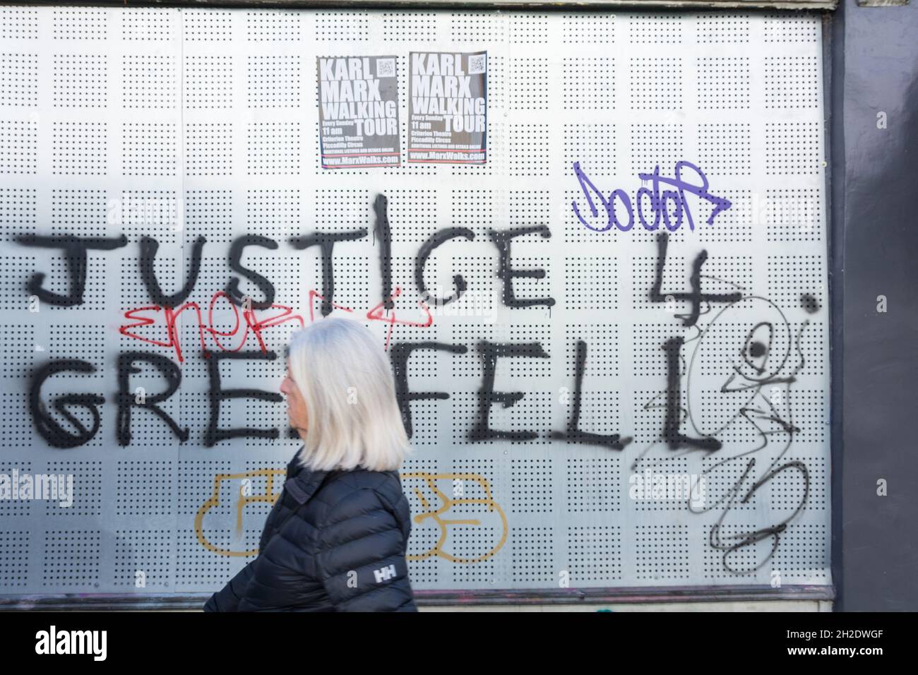 Una donna che passa davanti a Justice for Grenfell Graffiti su Westbourne Grove, Londra, Inghilterra, Regno Unito Foto Stock