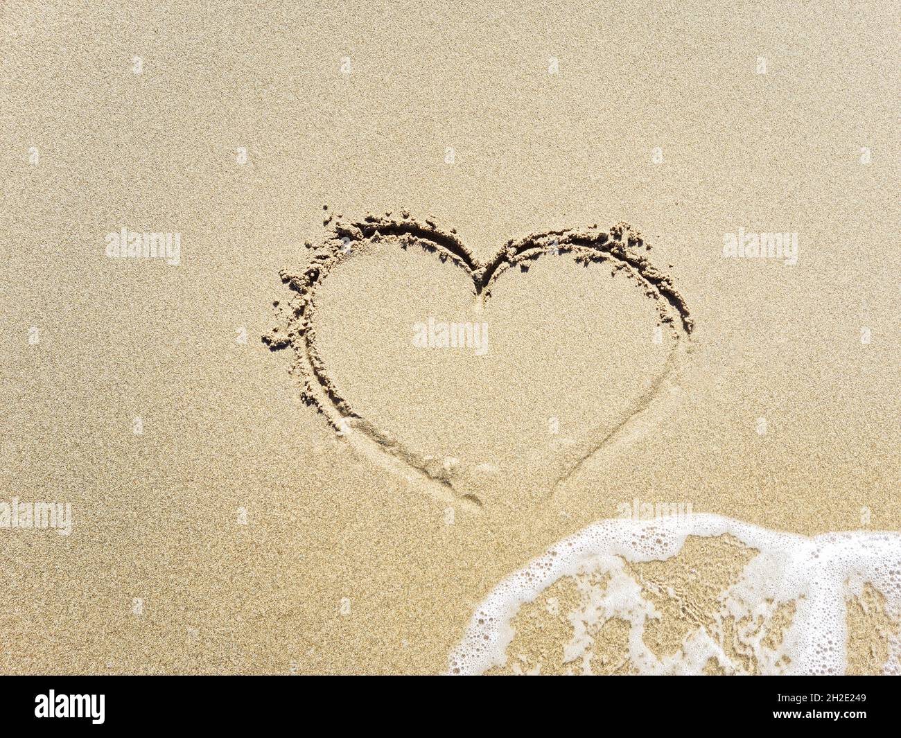 Il cuore nella sabbia è lavato via dall'onda. Foto Stock