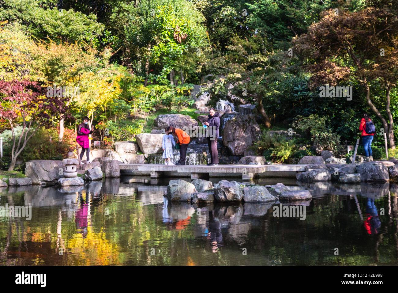 Holland Park, Londra, Regno Unito. 21 ottobre 2021. Le persone ammirano il paesaggio acquatico al Kyoto Garden in Holland Park, un giardino giapponese progettato per portare il paesaggio giapponese a Londra. Gli alberi del giardino stanno cominciando a mostrare i loro bei colori autunnali nell'odierno sole grazioso. Credit: Imagplotter/Alamy Live News Foto Stock