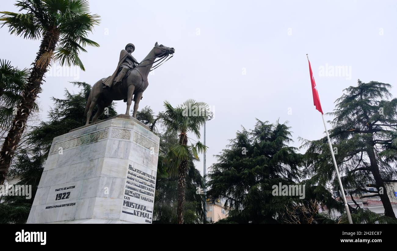 Ataturk fondatore della Repubblica Turca nel centro di Bursa (heykel) durante il tempo piovoso e coperto con bandiera turca e scultura ricoperta da alberi Foto Stock