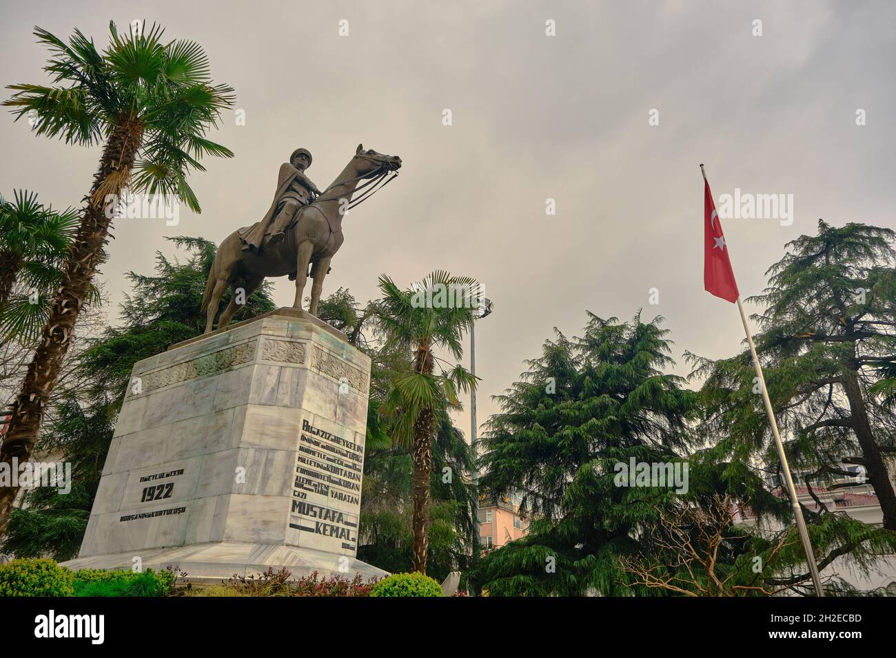 Ataturk fondatore della Repubblica Turca nel centro di Bursa (heykel) durante il tempo piovoso e coperto con bandiera turca e scultura ricoperta da alberi Foto Stock