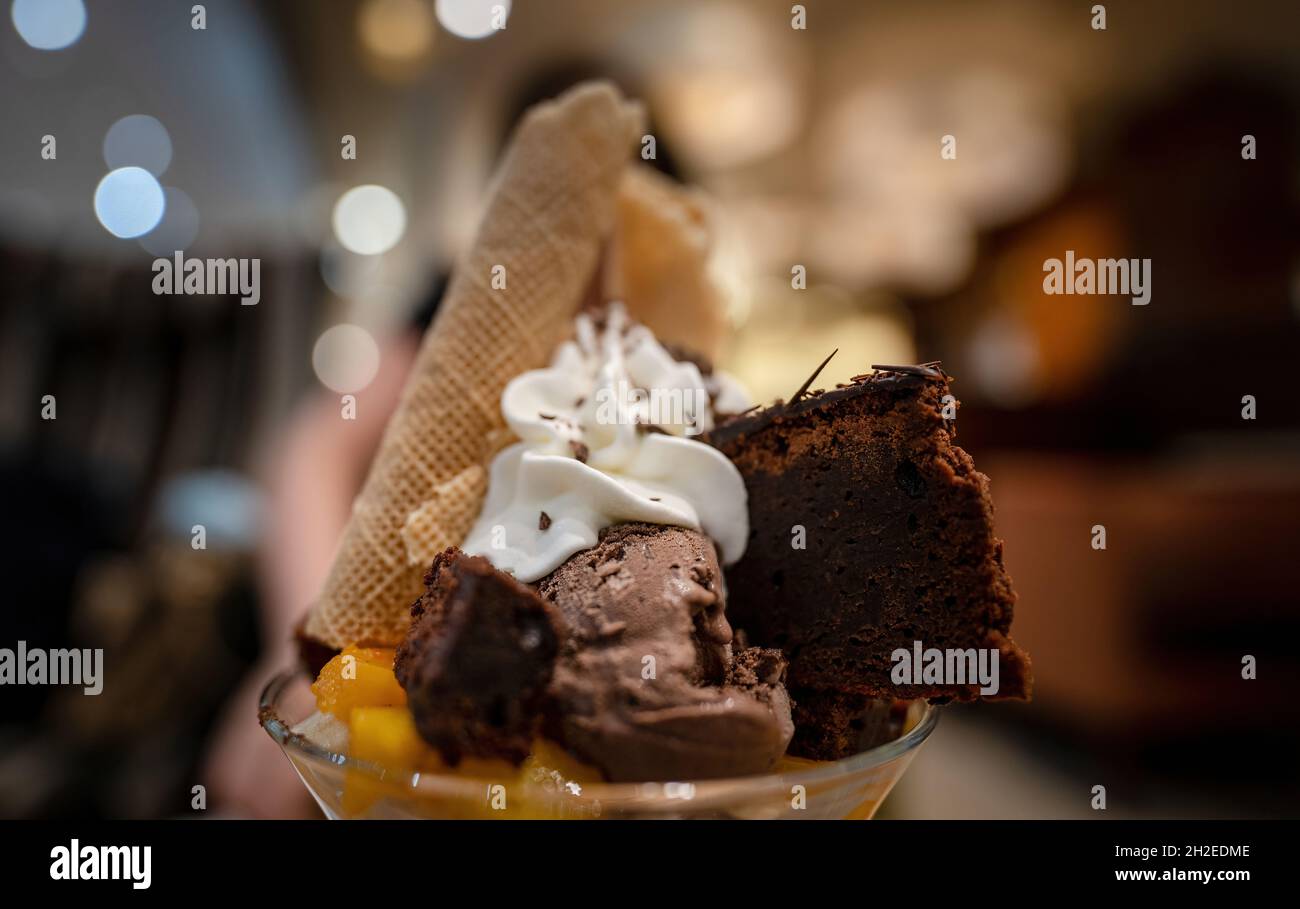 Pezzi di brownie caldo con gelato al cioccolato brownie, stracciatella e sorbetto al lampone con panna montata su sfondo sfocato. Selettivo per Foto Stock