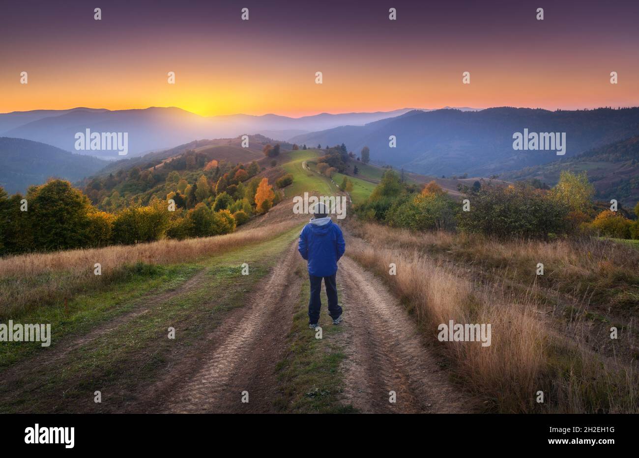 Uomo sulla strada sterrata rurale sulla collina guardando sulla montagna in nebbia Foto Stock