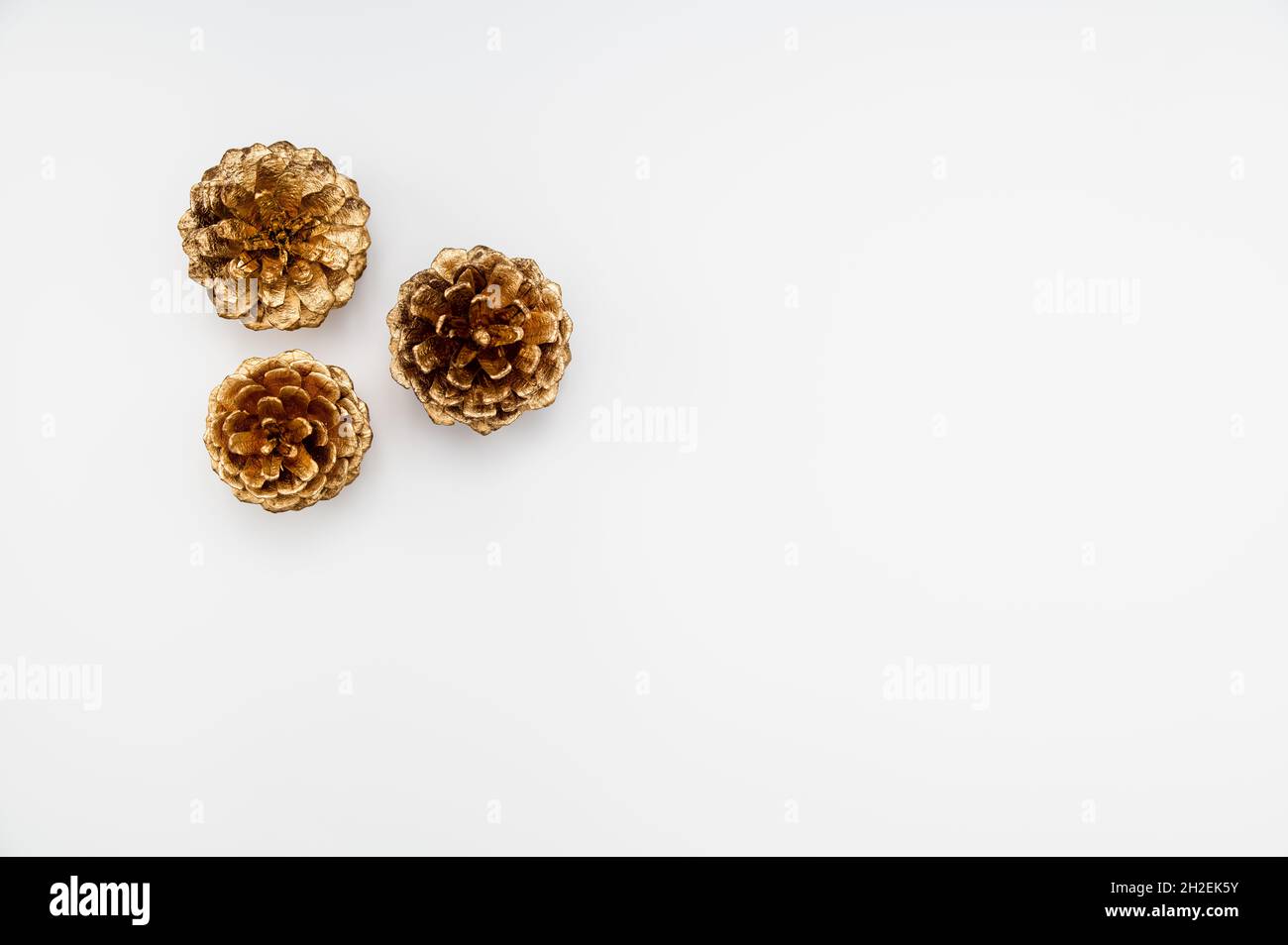 Concetto di Natale o inverno. Disposizione minimalista di tre coni di pino dorato su sfondo bianco. Foto Stock