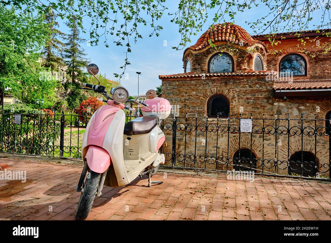 Piccolo mobiletto e scooter in stile vintage e retrò di colore rosa in piedi sul sentiero di ciottoli e di fronte alla moschea di hagia sophia a Nicea Foto Stock