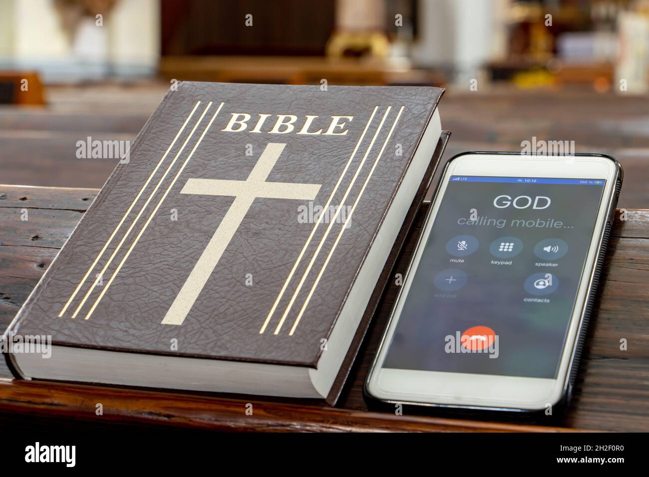 La Bibbia con telefono cellulare sul tavolo di una panchina di preghiera nella chiesa. Foto Stock