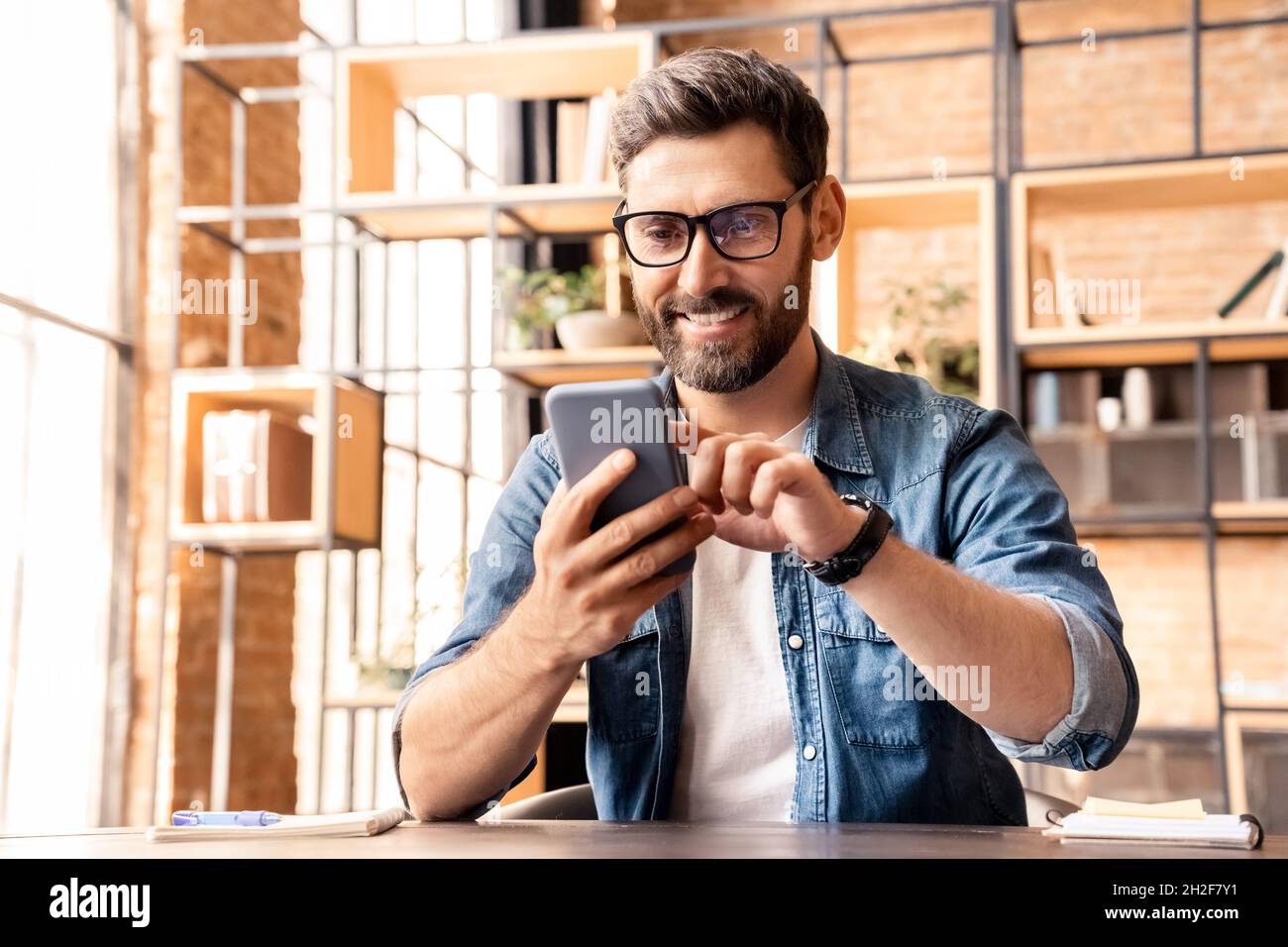 Ritratto di un uomo caucasico eccitato che utilizza lo smartphone mentre si riposa in ufficio Foto Stock