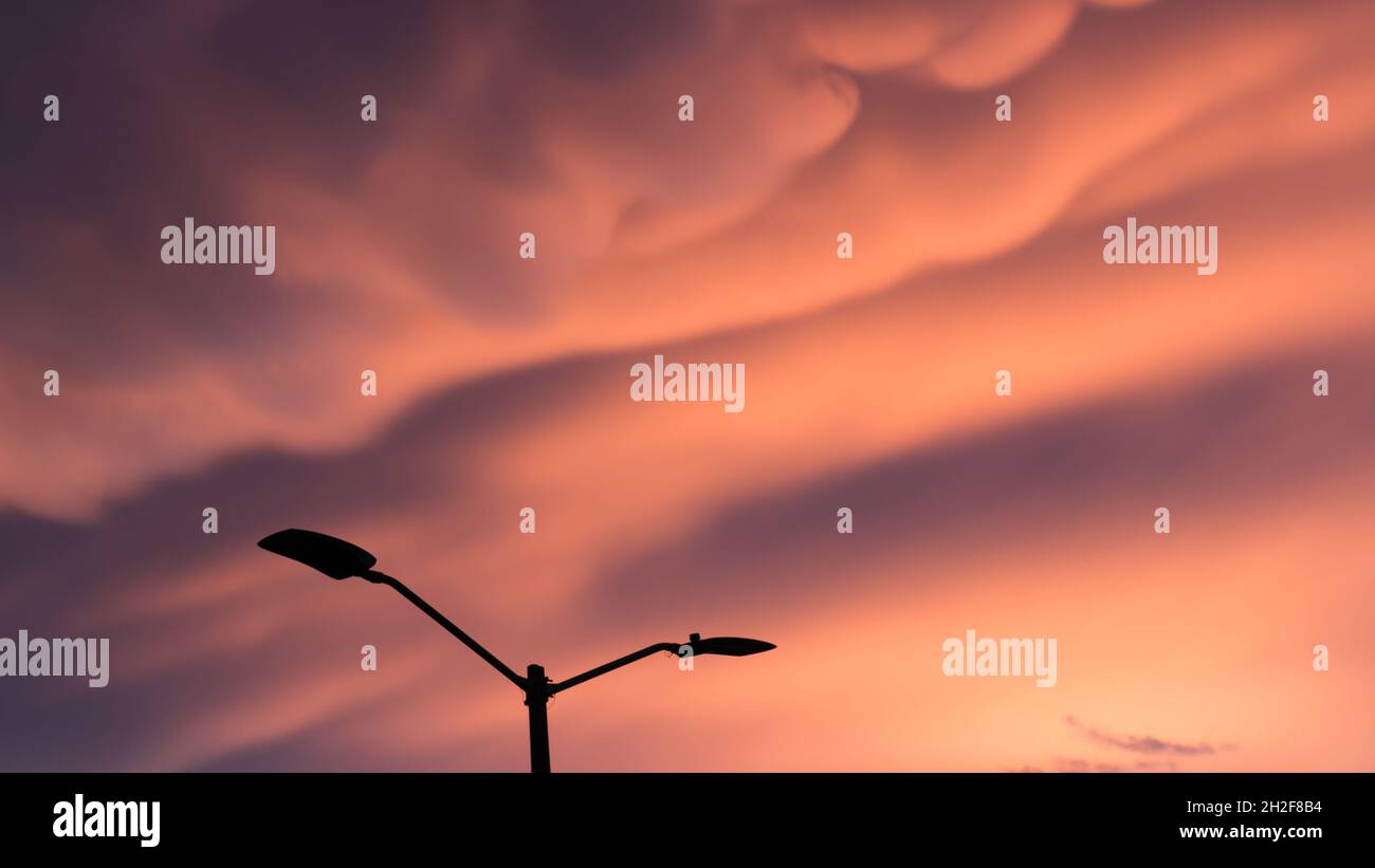 Silhouette con lampione di fronte a un incredibile tramonto in città con nuvole di caramelle in cotone Foto Stock