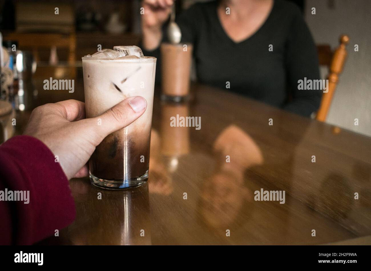 Bere caffè ghiacciato al tavolo con donna bianca di mezza età Foto Stock