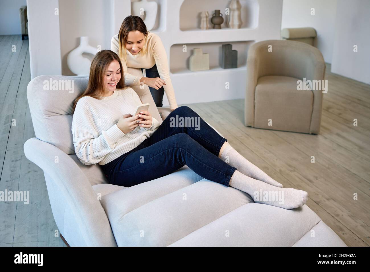 Due donne in chaise longue con telefono in salotto. Foto Stock