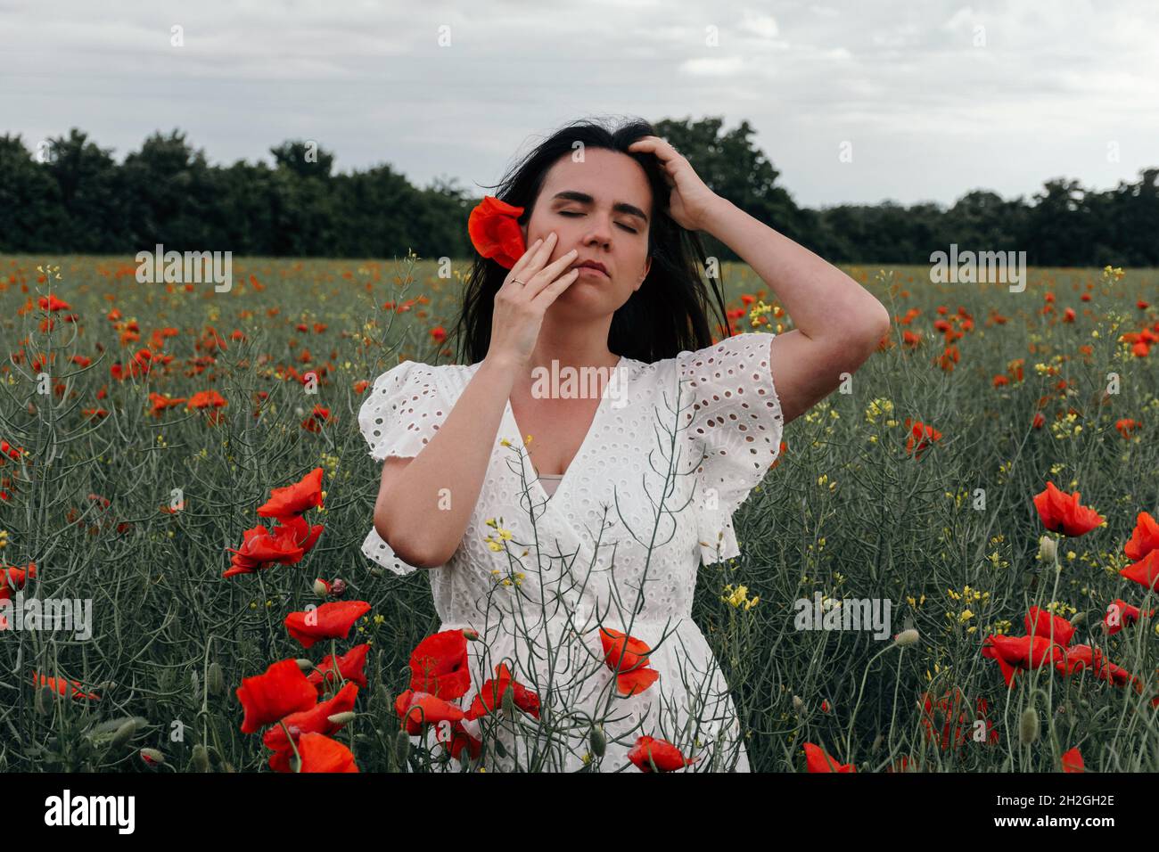 Bella giovane donna vestita bianca, in piedi in campo papavero Foto Stock