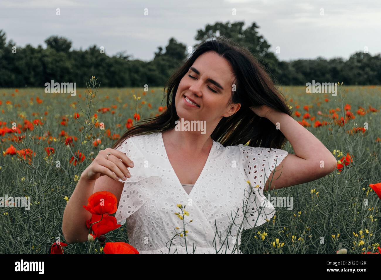 Bella giovane donna vestita bianca, in piedi in campo papavero Foto Stock