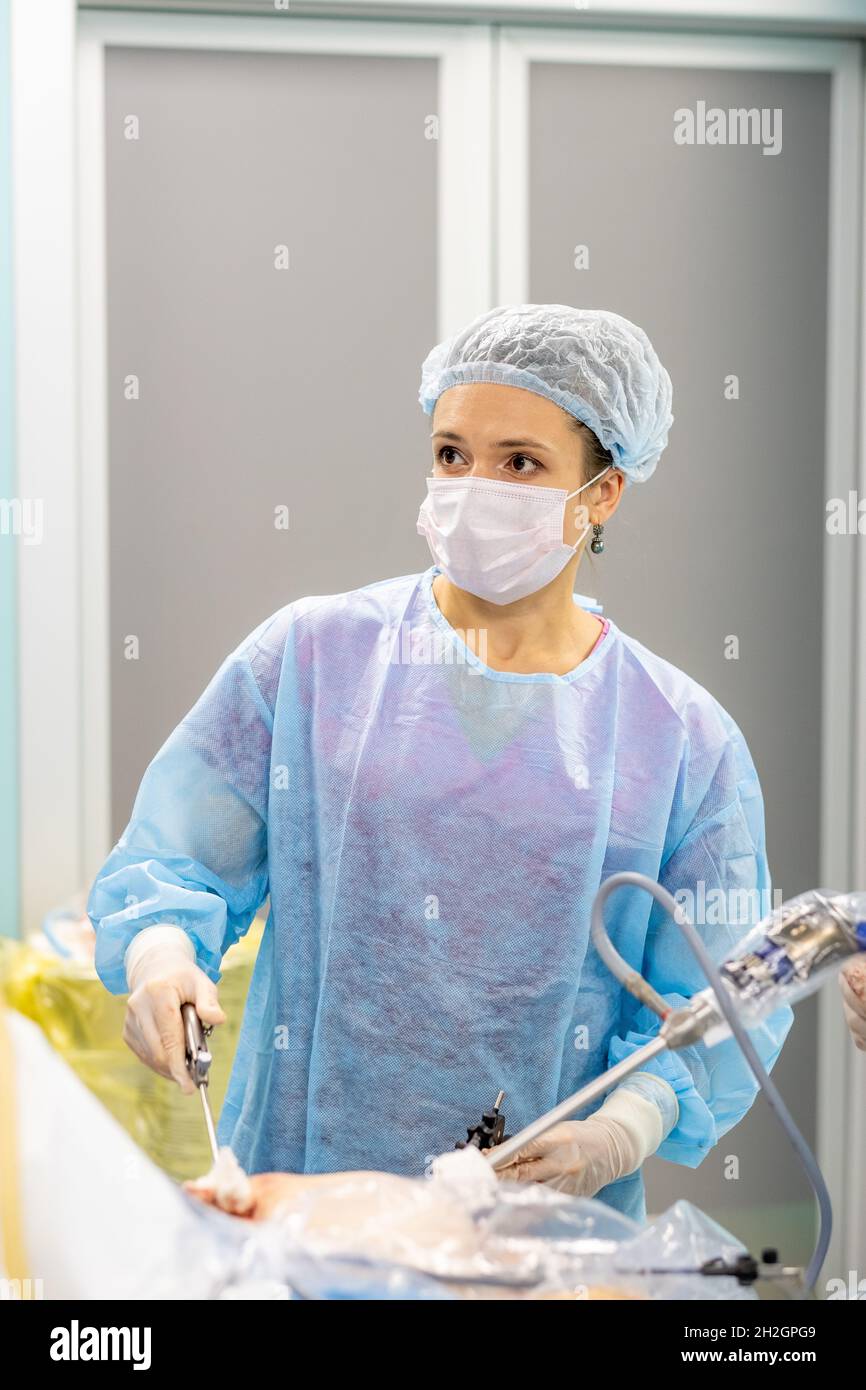 Una chirurgo femminile esegue un'operazione laparoscopica minimamente invasiva. Un medico in una uniforme chirurgica e una maschera medica opera un paziente con manipolatori laparoscopici. Messa a fuoco selettiva. Foto Stock