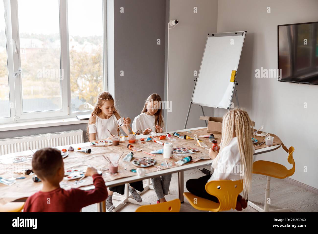 Bambini seduti al tavolo e disegnando entusiasticamente con acquerelli su carta Foto Stock