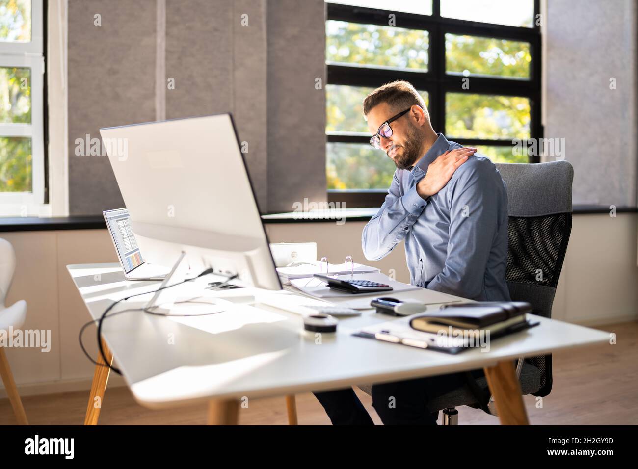 Dolore alle spalle e postura. Uomo che soffre vicino computer workstation Foto Stock