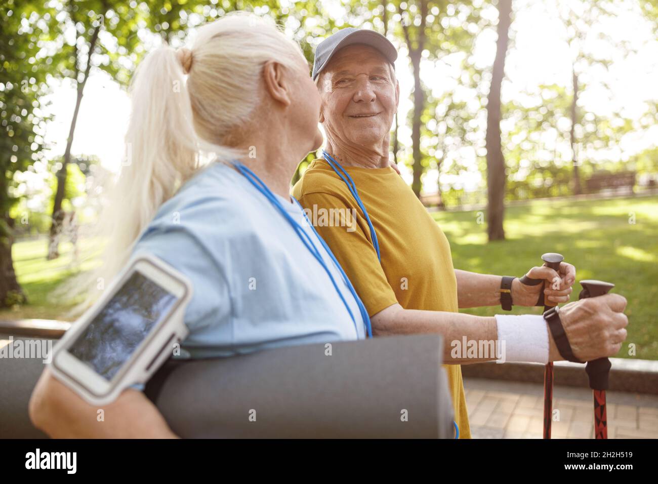 Uomo anziano allegro con pali per nordic walking e donna nel parco verde Foto Stock