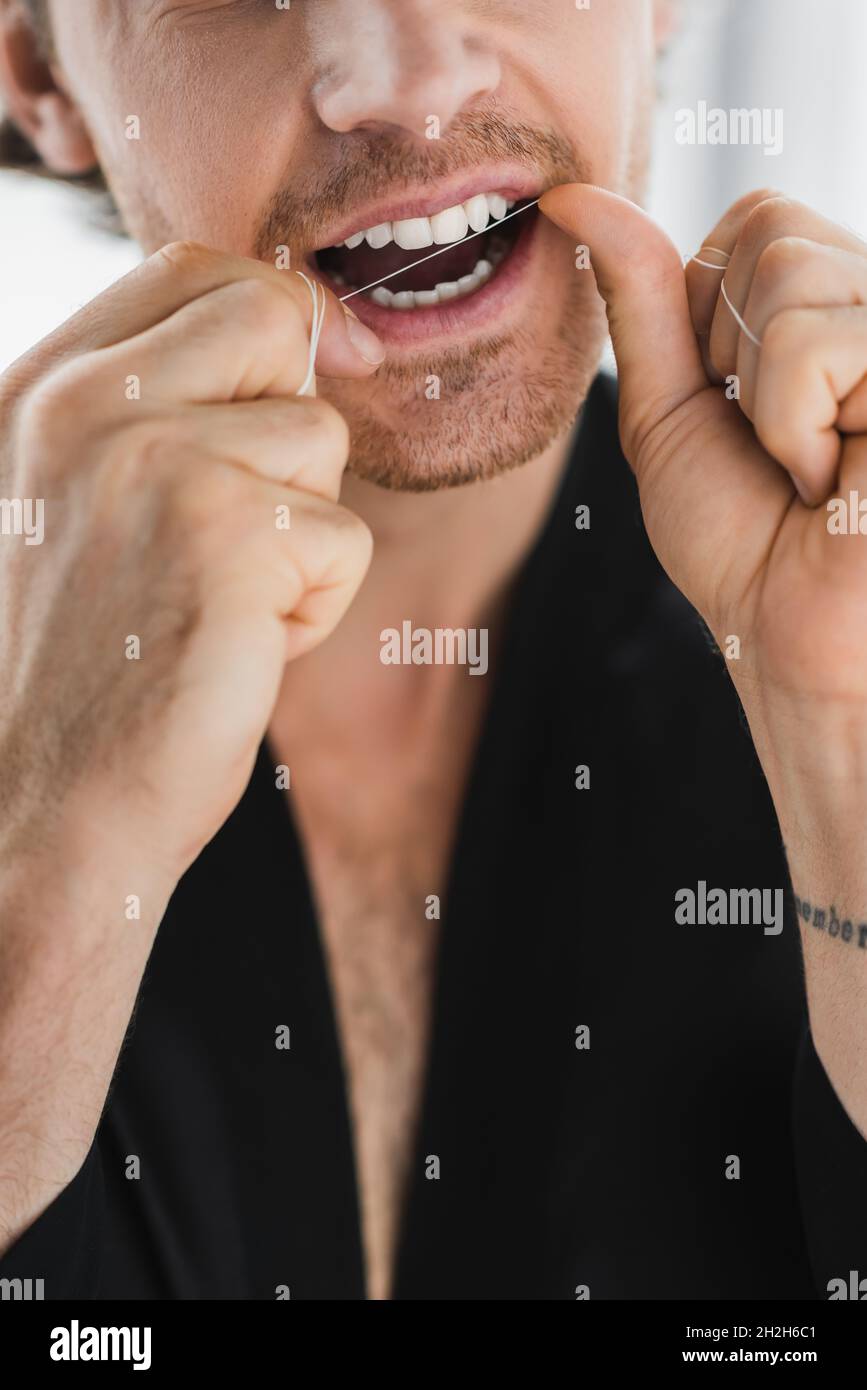 Vista ritagliata dell'uomo in nero accappatoio pulizia denti con filo interdentale Foto Stock