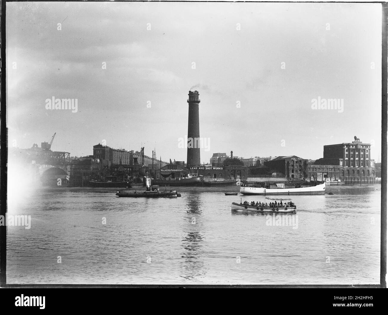 Shot Tower and Lead Works, Belvedere Road, Lambeth, Greater London Authority, 1936. Una vista sul Tamigi verso la torre dei colpi di Lambeth Lead Works, e in primo piano, una barca passeggeri o traghetto che viaggia lungo il fiume. La torre di tiro dei Lambeth Lead Works fu progettata da David Ridall Roper e fu costruita nel 1826 per Thomas Maltby & Co. Al tempo di questa fotografia fu gestita da Walkers, Parker & Co, ma fu demolita nel 1962 per fare posto alla Sala della Regina Elisabetta. Foto Stock