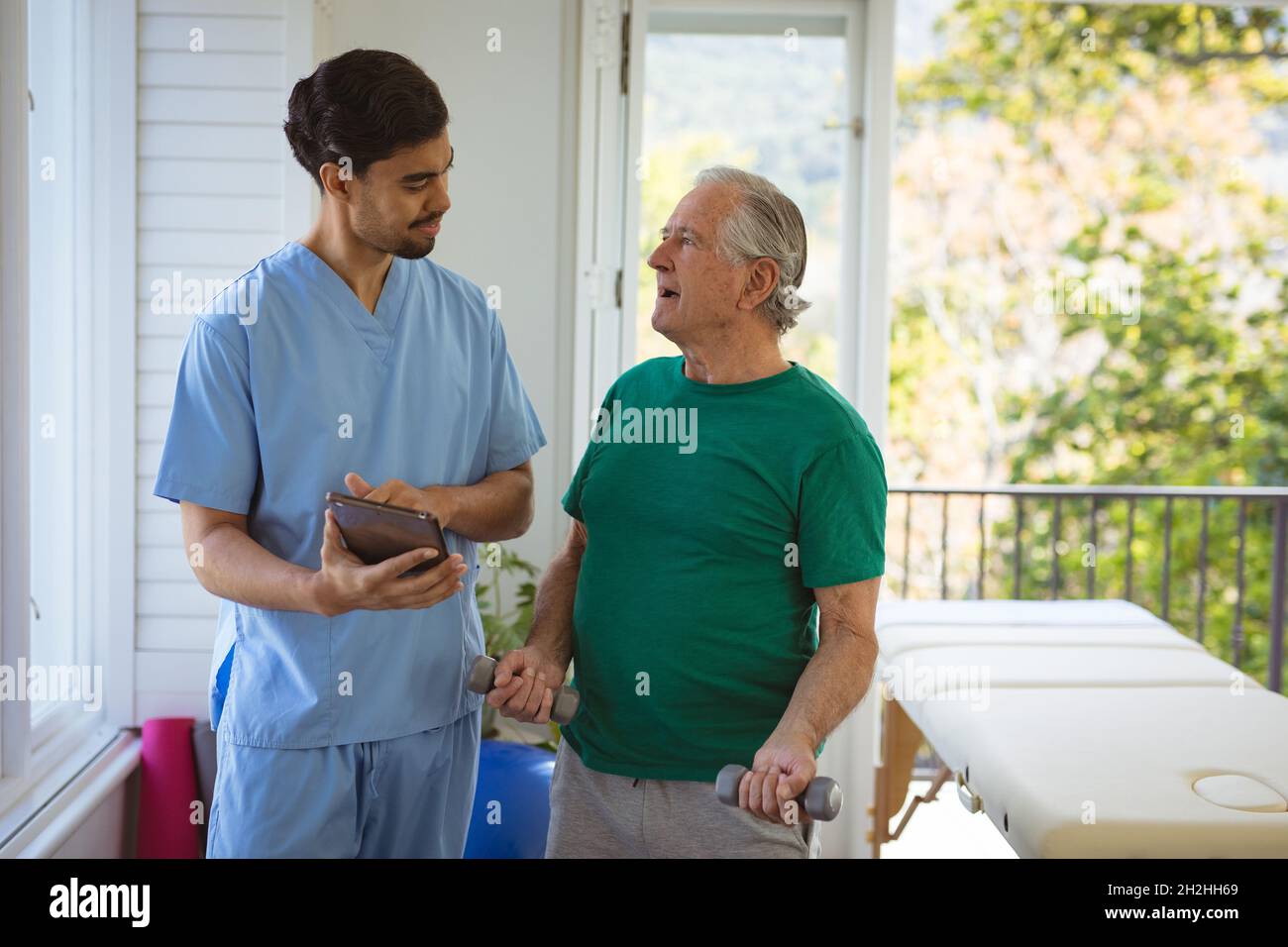 Fisioterapista di sesso maschile che tratta le braccia di un paziente di sesso maschile anziano e usando una compressa in clinica Foto Stock