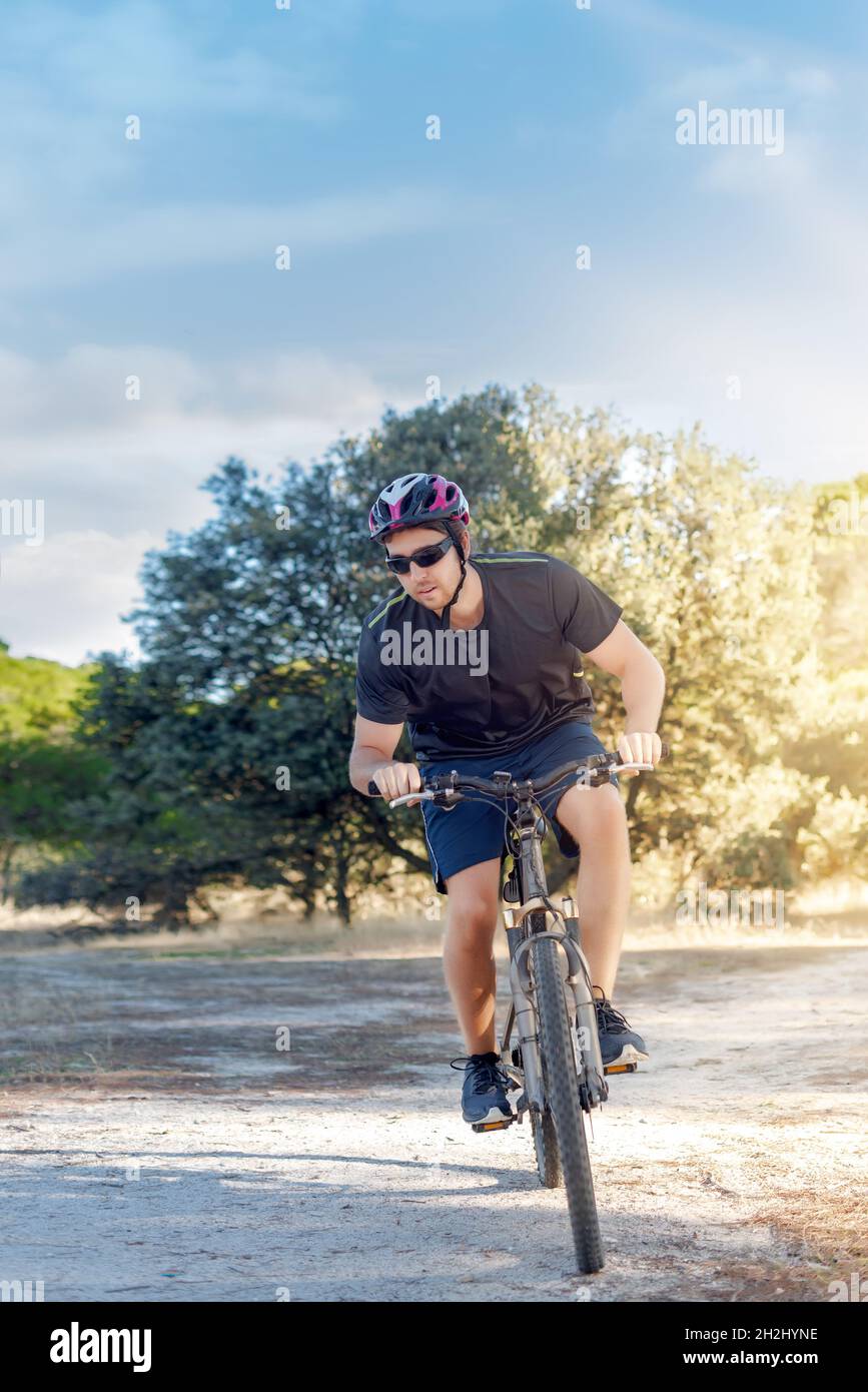 Ciclista maschile che guida la sua bicicletta in campagna al tramonto. Corsa in mountain bike nella foresta Foto Stock