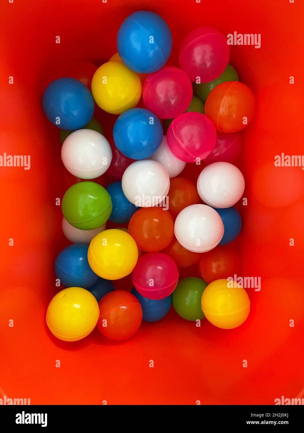 Vista dall'alto di molte palline di plastica colorate in contenitore rosso nella stanza dei bambini Foto Stock