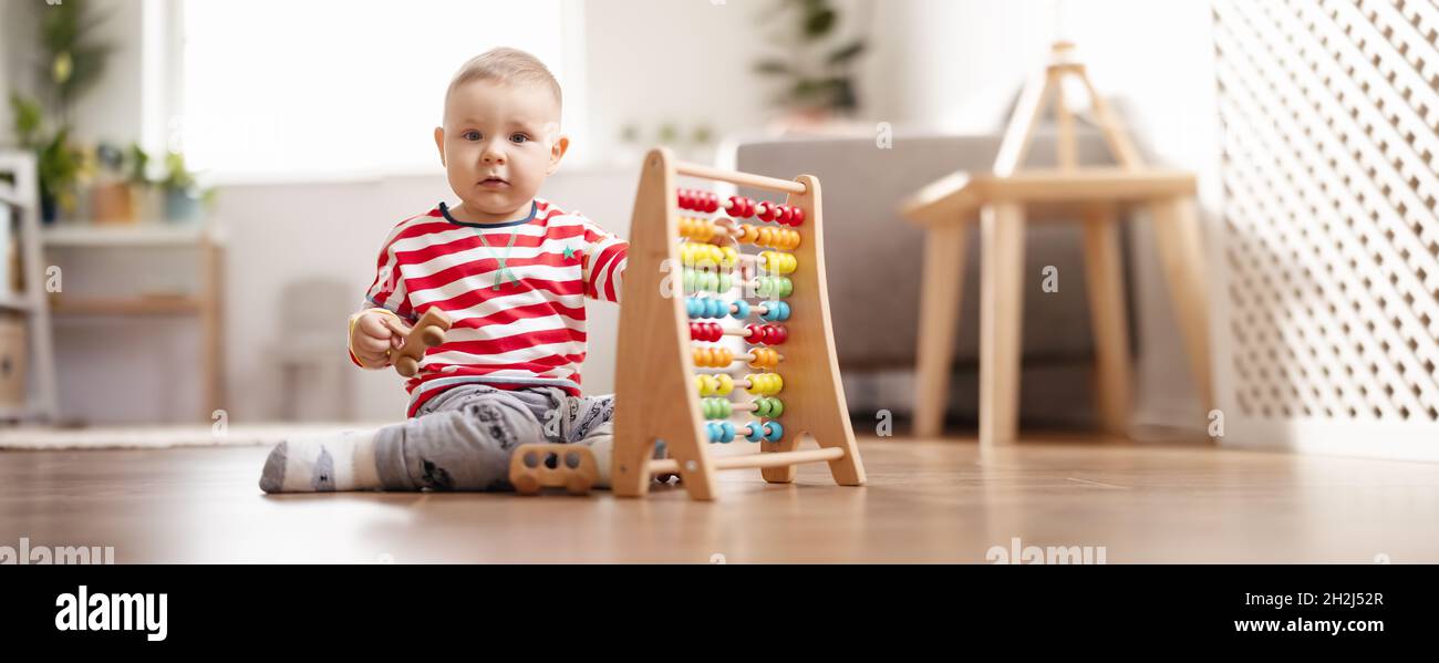 Bambino carino seduto sul pavimento in camera e giocare con i giocattoli. Foto Stock
