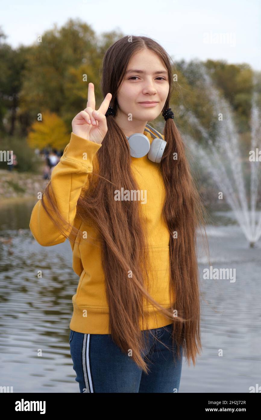 Una ragazza adolescente con capelli lunghi e cuffie mostra un gesto di due dita. Foto Stock