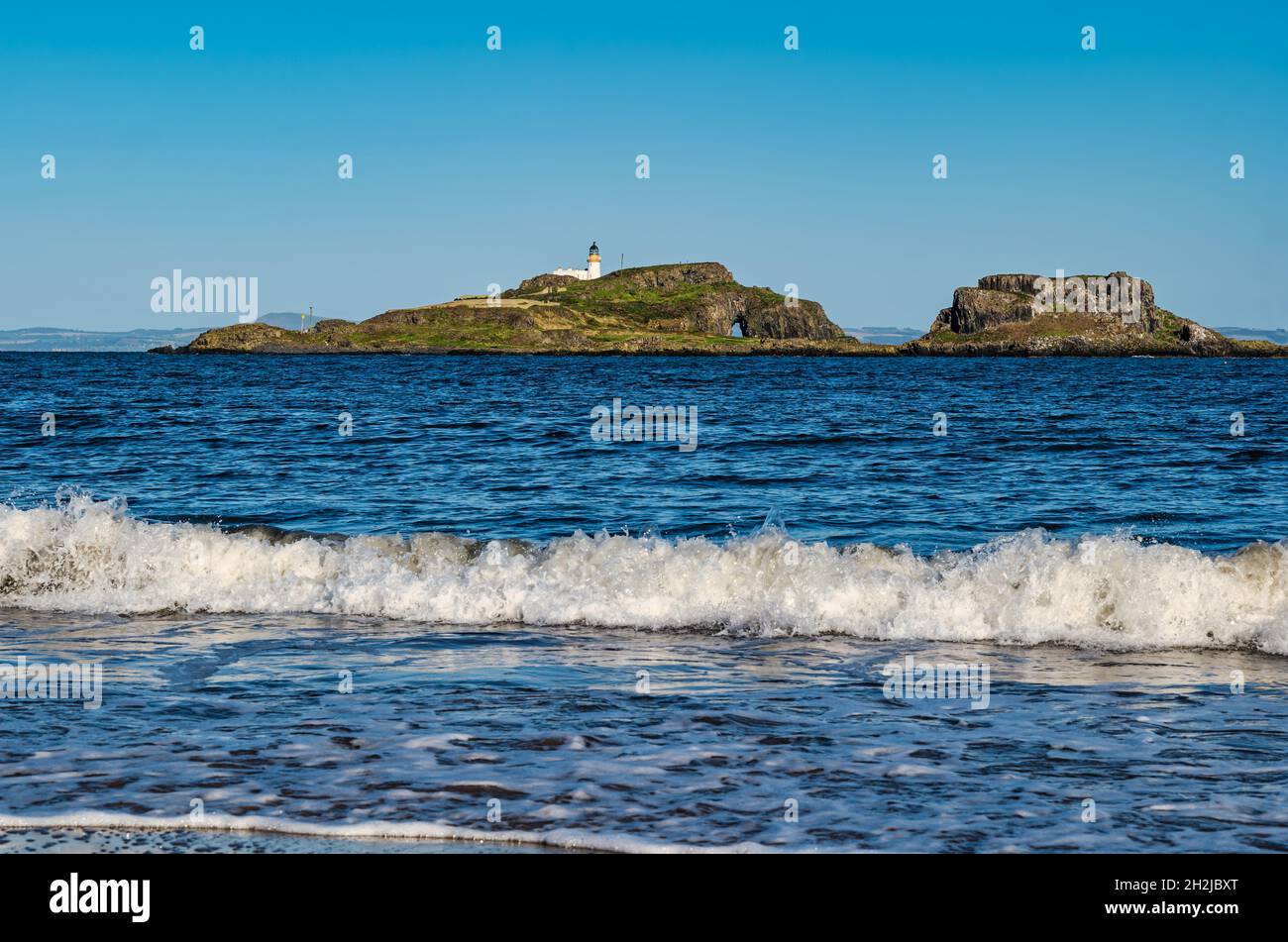 Ondate che si infrangono sulla riva della spiaggia di Yellowcraig con vista sul faro dell'isola di Fidra in giornata di sole, East Lothian, Scozia, Regno Unito Foto Stock