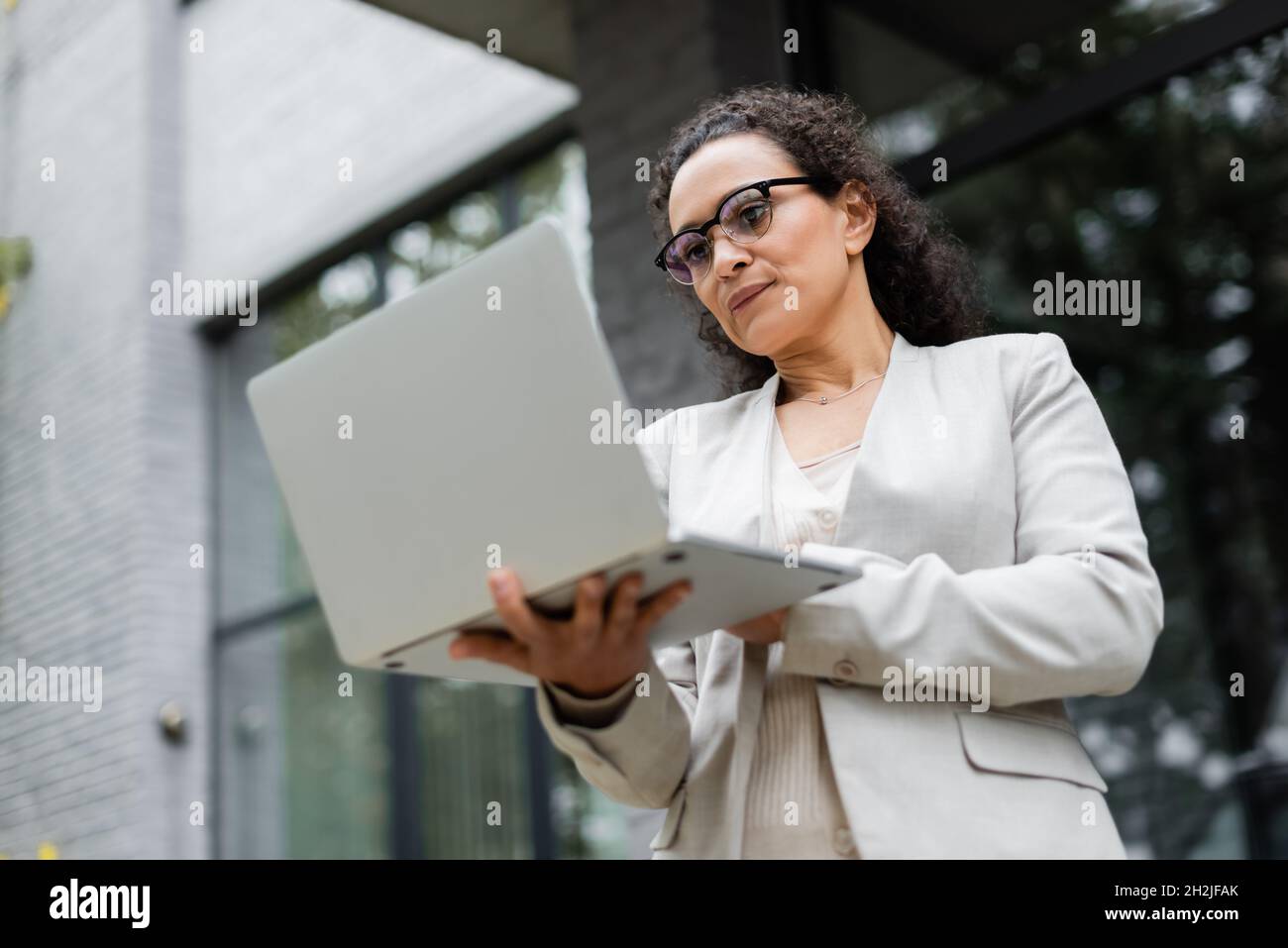 vista ad angolo basso di una pensierosa donna d'affari afroamericana che guarda il computer portatile sulla strada della città Foto Stock