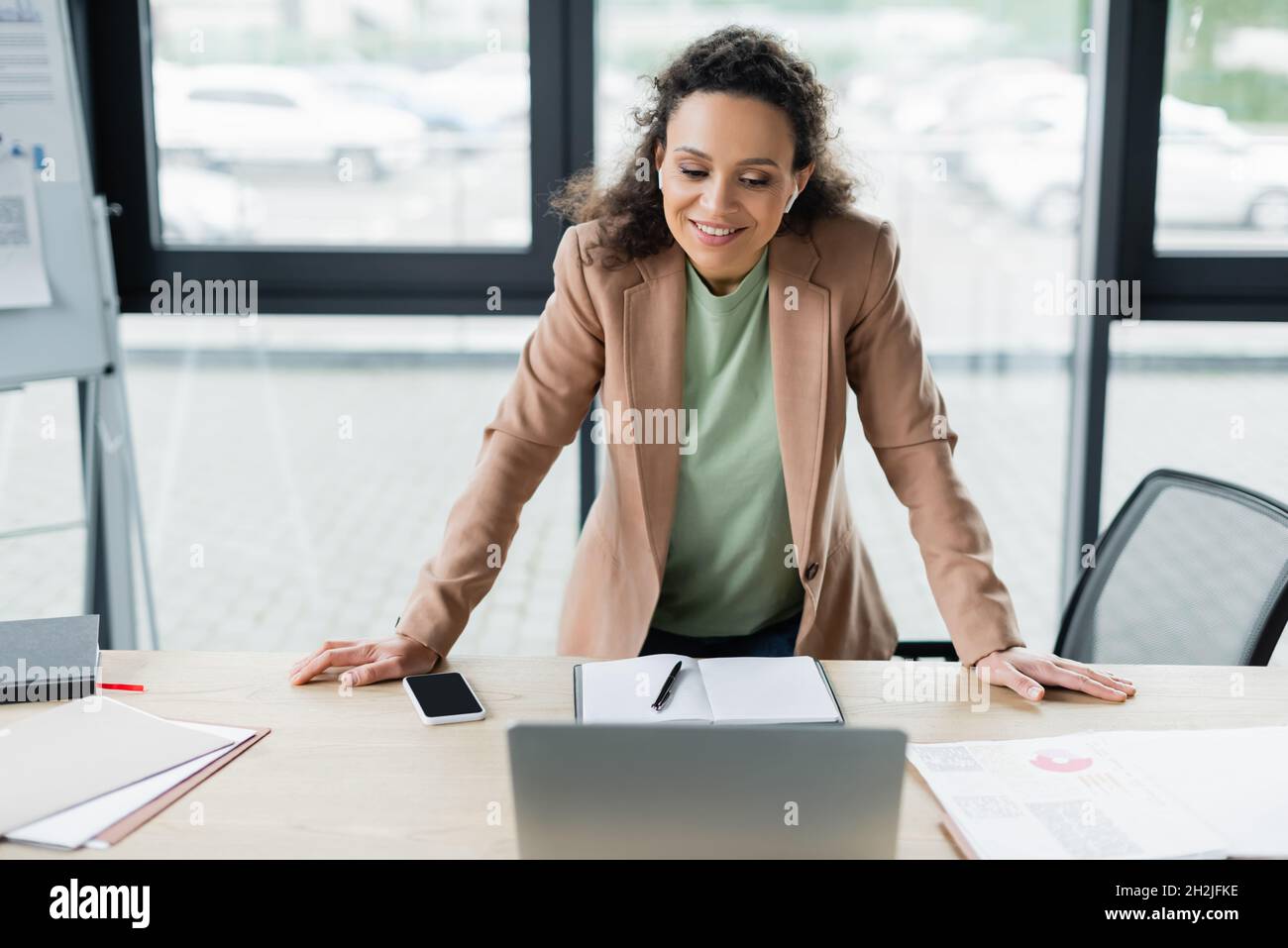 una donna d'affari afroamericana sorridente in piedi alla scrivania durante la videoconferenza su un laptop sfocato Foto Stock