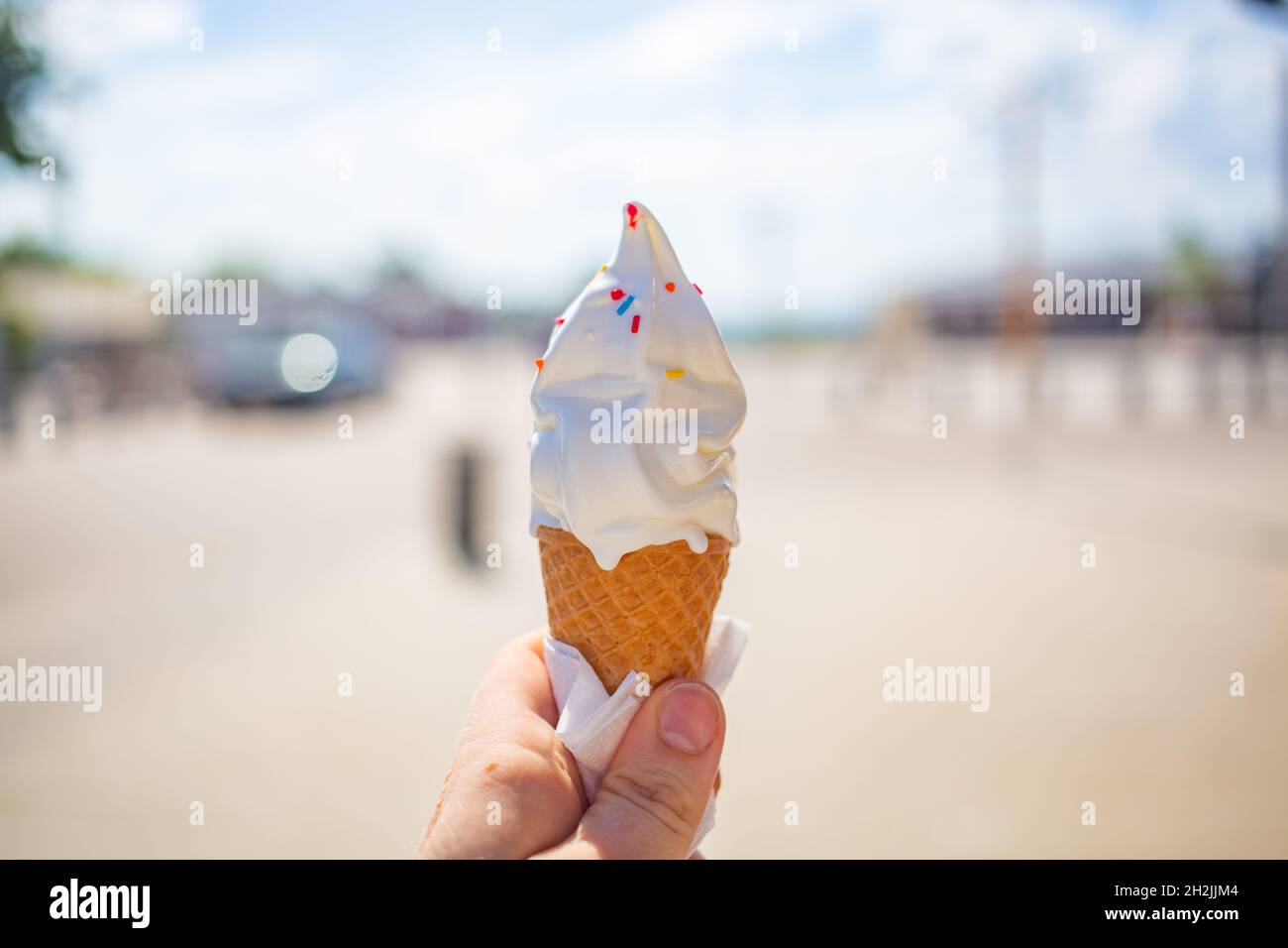 Una mano femmina tiene un cono gelato su un bacground di strada. Il gelato si sciolse e scese le dita e la mano. Una giornata calda fuori. Primo piano, no Foto Stock