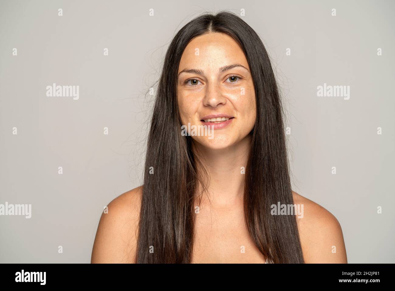 una giovane donna sorridente senza trucco con capelli lunghi su sfondo grigio Foto Stock