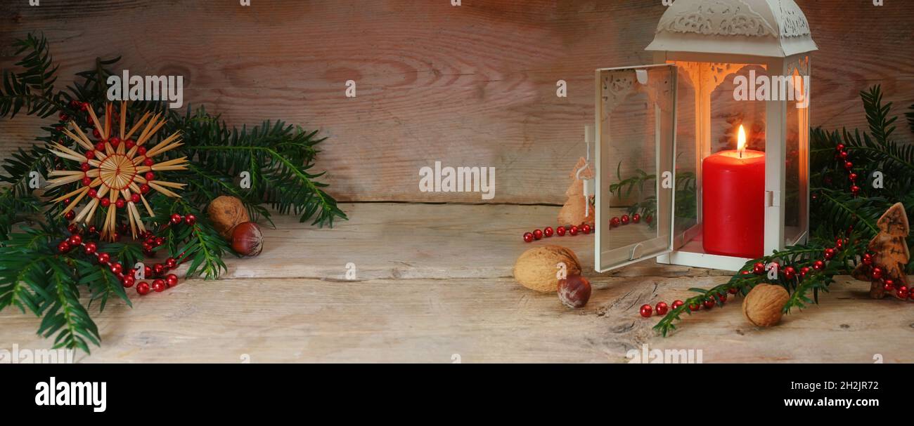 Candela rossa con luce calda in lanterna, decorazione e rami sempreverdi su tavole rustiche di legno per Natale e Avvento, formato panoramico, copia sp Foto Stock