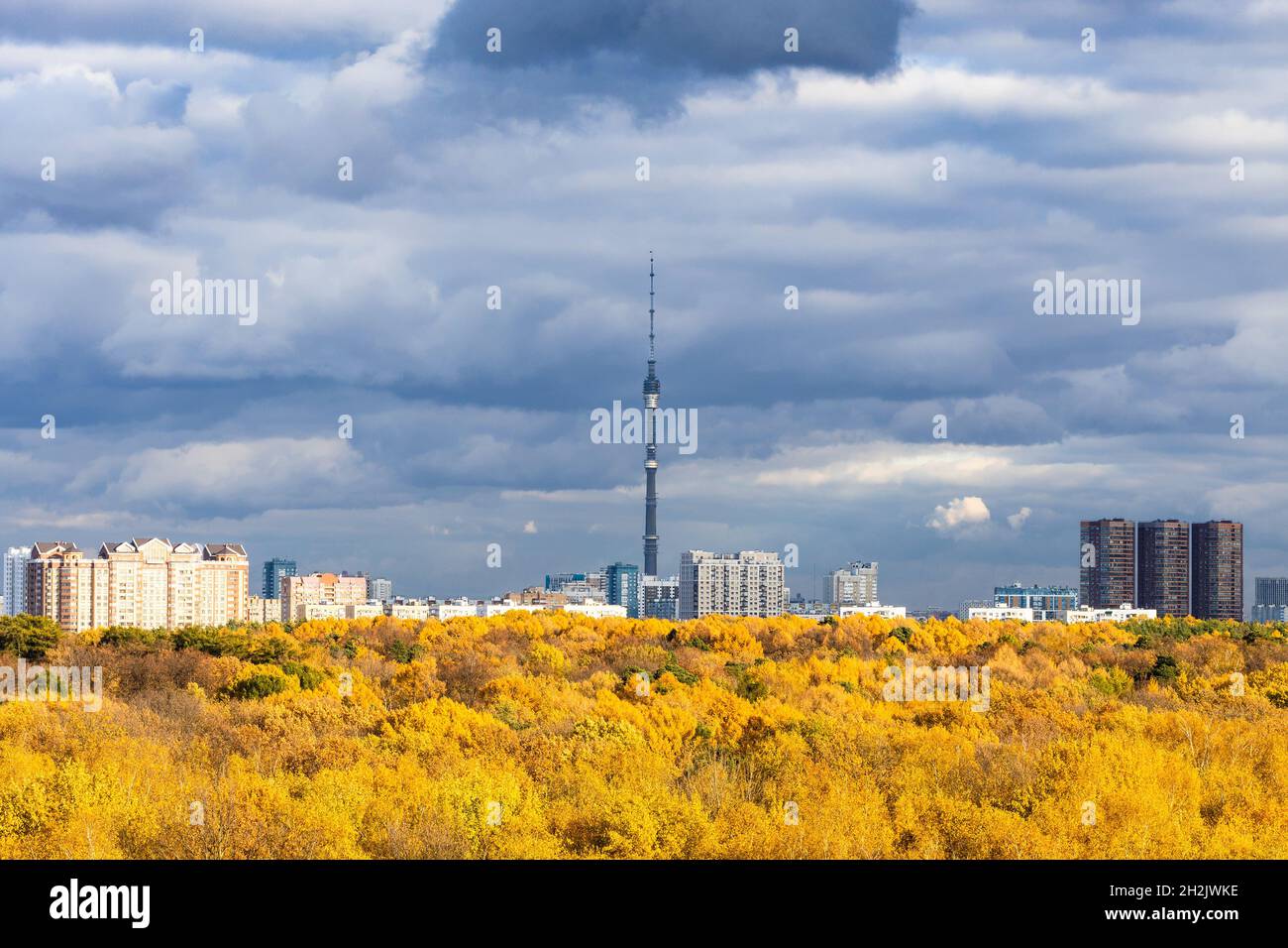 Le nuvole di pioggia grigio scuro nel cielo blu sopra la città con la torre della televisione e la foresta gialla illuminata dal sole il giorno d'autunno prima della pioggia Foto Stock