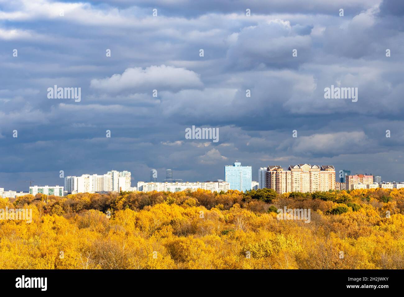 moderne case urbane e parco cittadino giallo illuminato dal sole sotto le nuvole di pioggia grigio scuro in cielo il giorno autunnale prima della pioggia Foto Stock