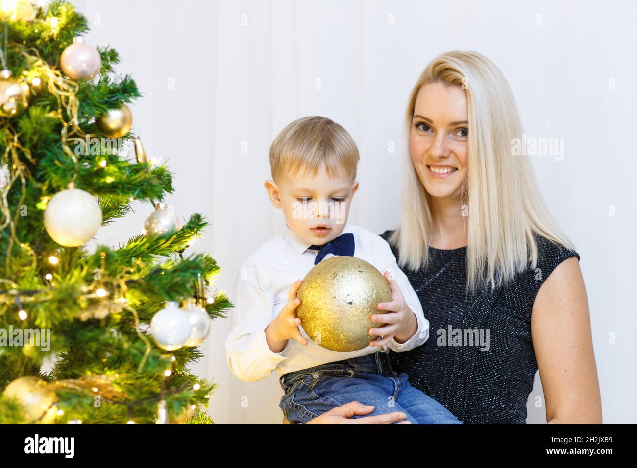 Madre e figlio che decorano albero di natale con palle d'oro e giocattoli. Natale con la famiglia. Foto Stock