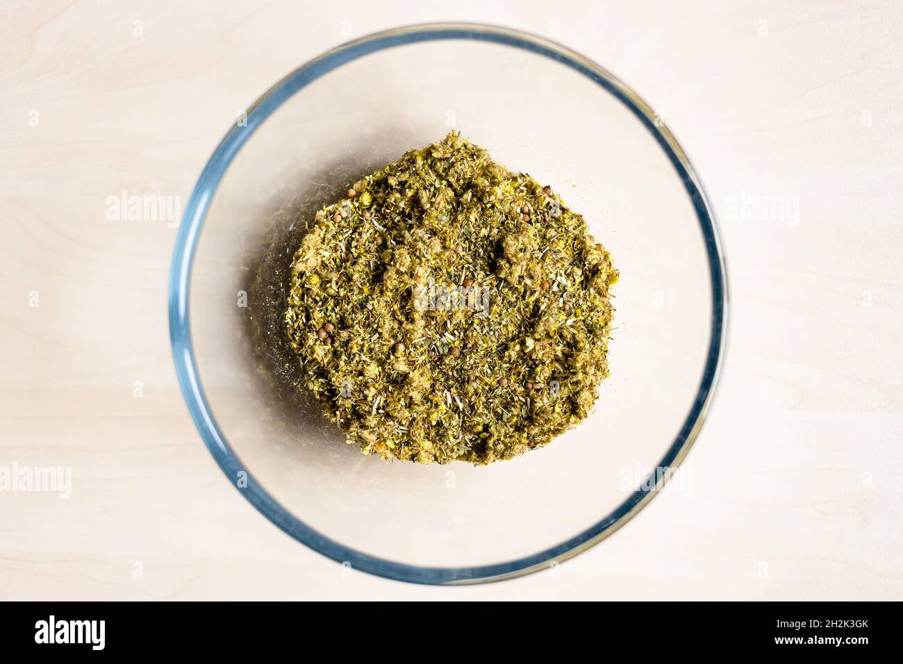 vista dall'alto della miscela secca di erbe medicinali e piante tritate in una ciotola di vetro su un tavolo marrone chiaro Foto Stock