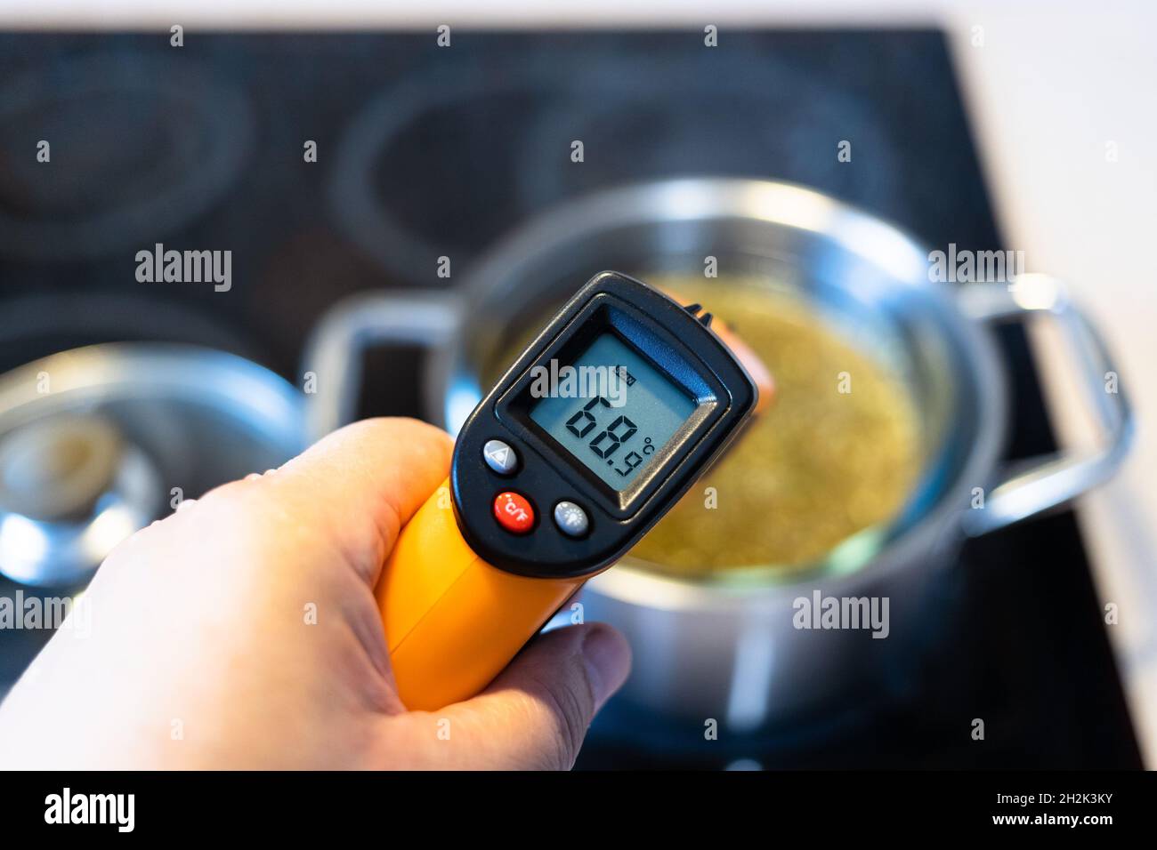 misurazione della temperatura della superficie dell'acqua durante la cottura a vapore tee di erbe in bagno d'acqua con termometro a infrarossi su stufa in ceramica in cucina a casa Foto Stock