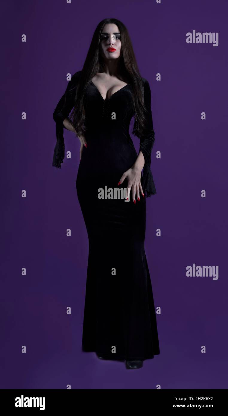 Bella ed esuberante donna con aspetto sinistro e scuro, guardando intensamente la macchina fotografica, con un vestito nero, lunghi capelli neri, chiodi pallidi e rossi. Foto Stock