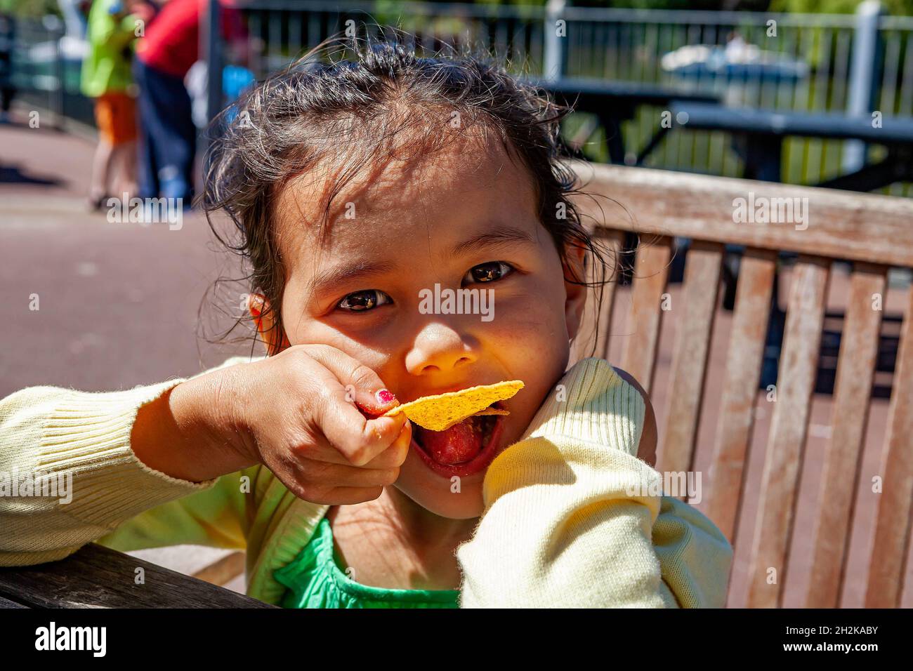 La giovane ragazza inglese/tailandese siede a una panchina e mangia una tortilla al campo di vacanze di Pwlllheli Foto Stock