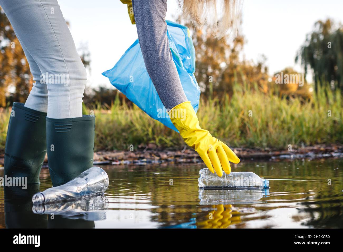 Pulizia ambientale. Volontario che raccoglie la bottiglia di plastica da fiume o lago inquinato. Inquinamento idrico con rifiuti di plastica Foto Stock