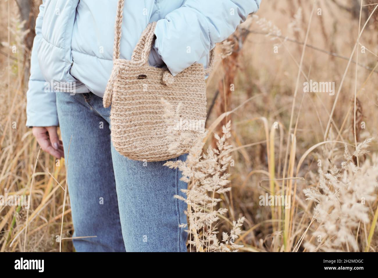 Borsa per lo shopping in maglia di iuta naturale fatta a mano, stile scandinavo, toni beige, accessori moda sostenibile. Stile di vita senza sprechi. Donna in piedi in un campo con borsa di iuta fai da te Foto Stock