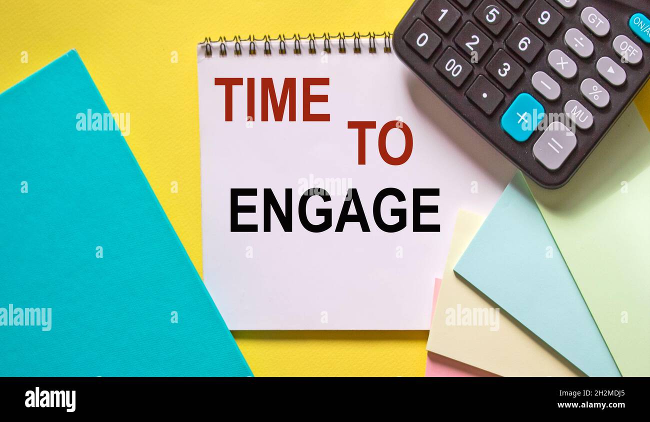 Tempo di coinvolgere , testo su un notebook, accanto a una calcolatrice, adesivi e diario su sfondo giallo Foto Stock
